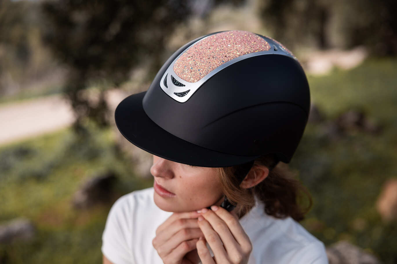 Frau stellt den Riemen eines stilvollen schwarzen Reithelms mit glitzerndem roségoldenem Einsatz ein.