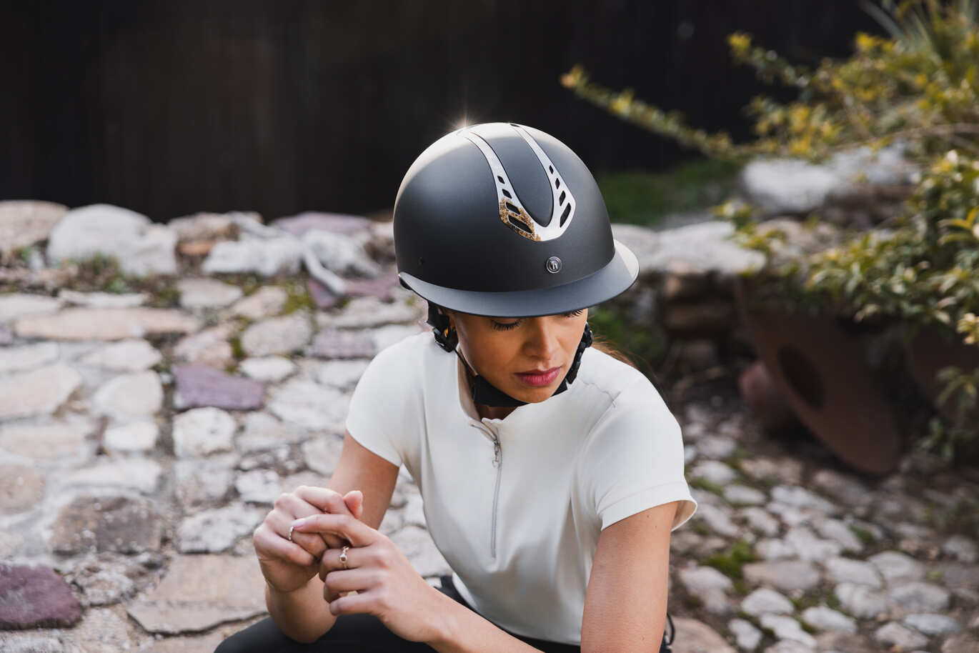 Frau in weißem Reitshirt trägt stilvollen schwarzen Reithelm mit silbernem Emblem